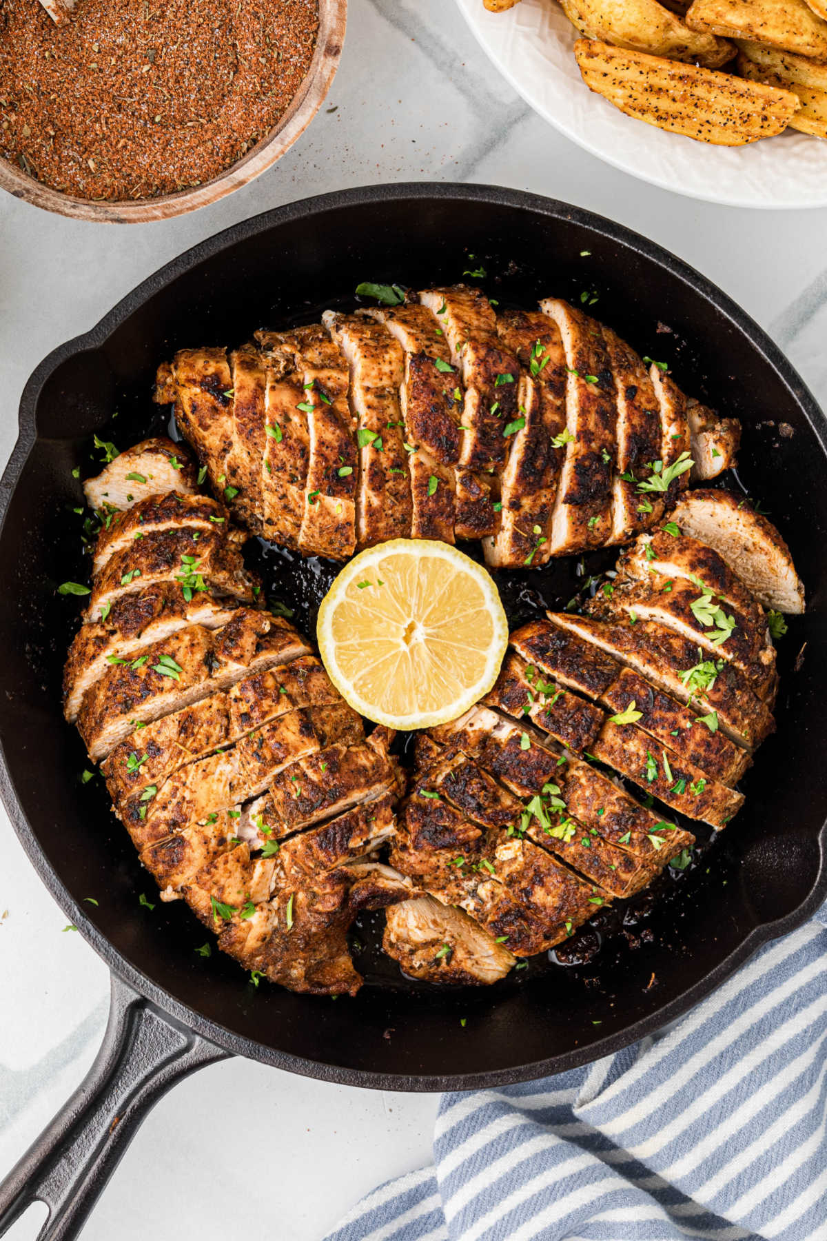 An overhead picture of a black cast iron skillet with three blackened chicken breasts, perfectly sliced, with a lemon half in the middle.