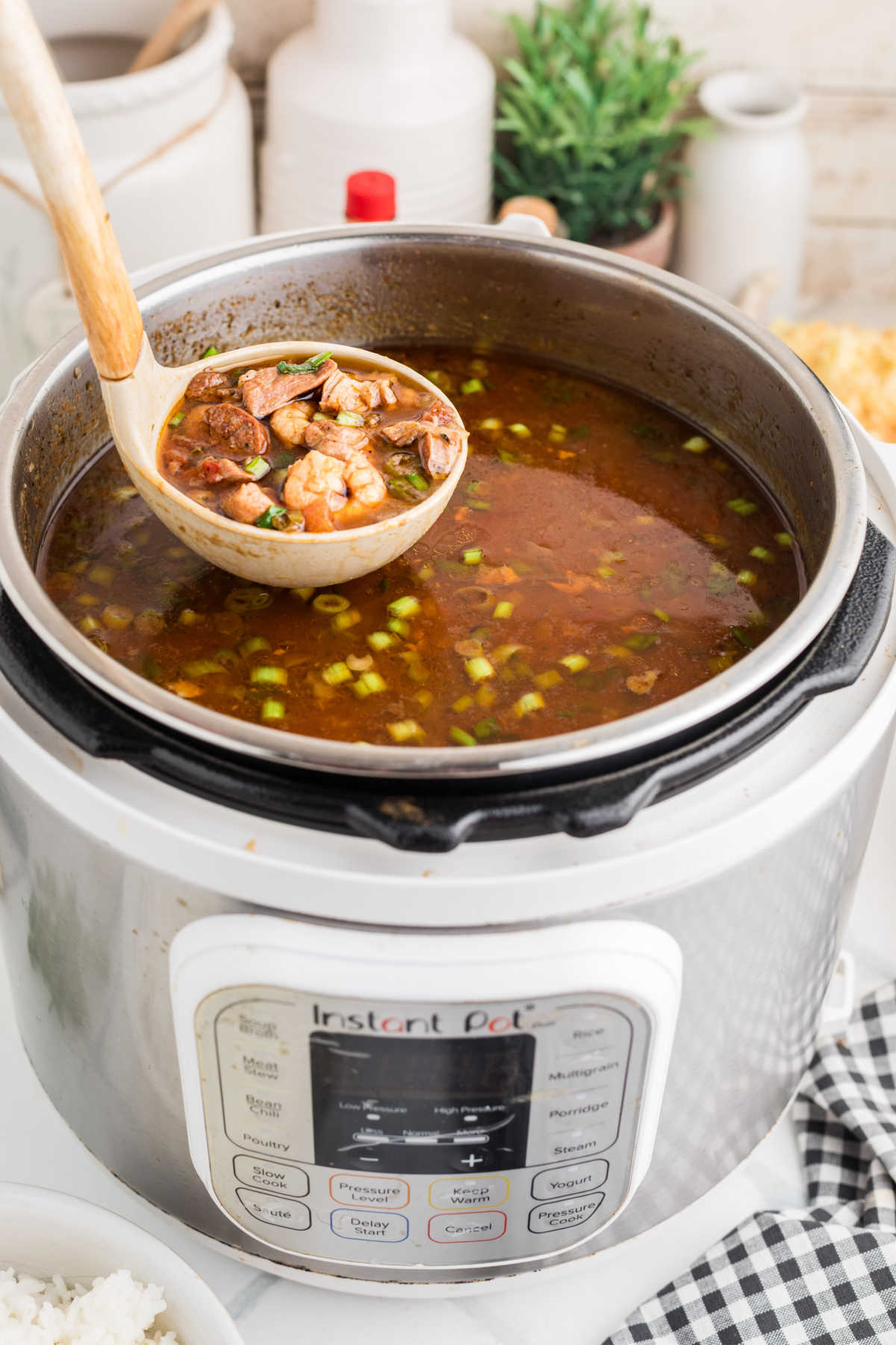 A ladle of gumbo being lifted out of a pressure cooker.
