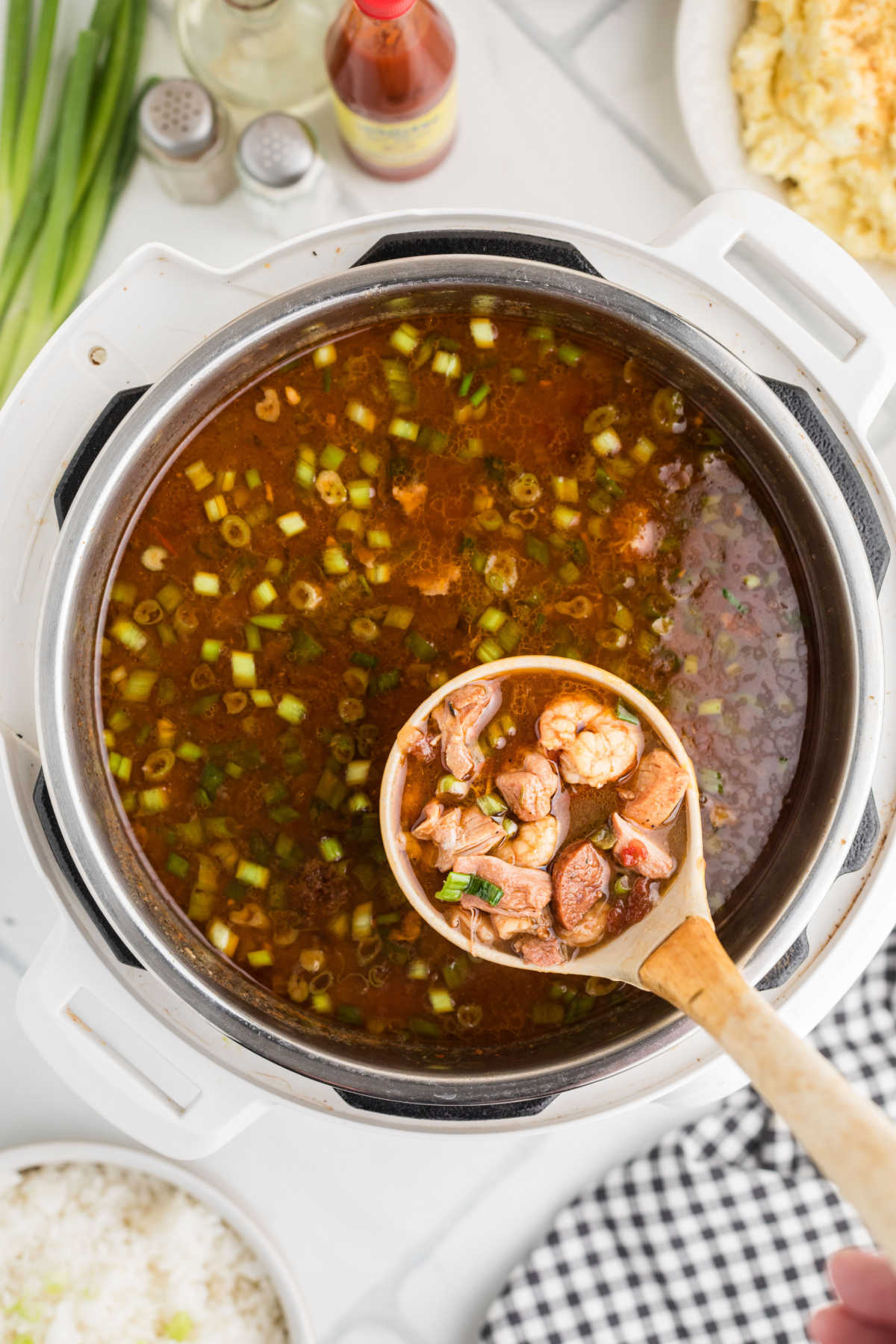 Overhead shot of a gumbo in a pressure cooker, a ladle full of gumbo being lifted out.